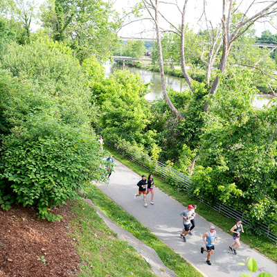Runners running on a greenway path next to the French Broad River in front of New Belgium Brewing